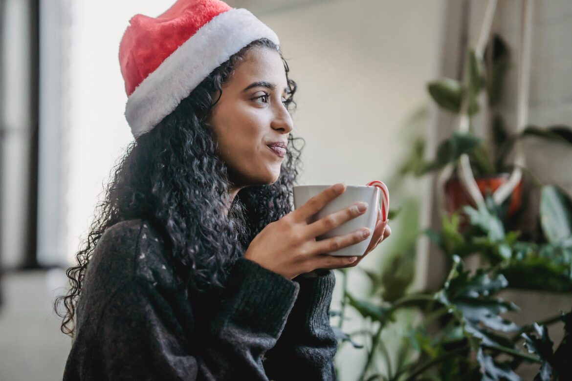 cheerful woman in christmas hat with hot cocoa at home