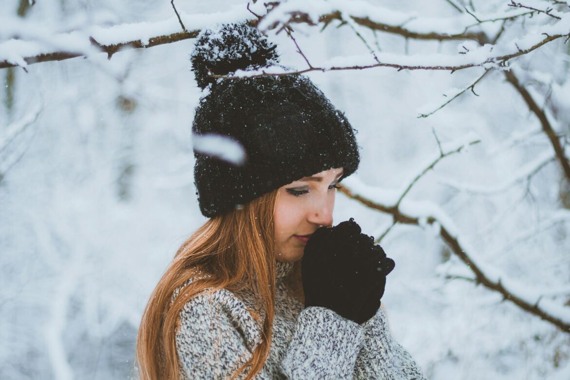 woman in winter forest holding hands together near face